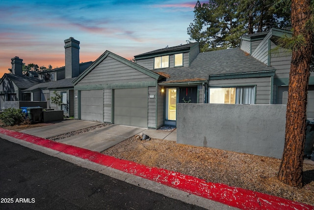 view of front facade with a garage, concrete driveway, a shingled roof, and fence