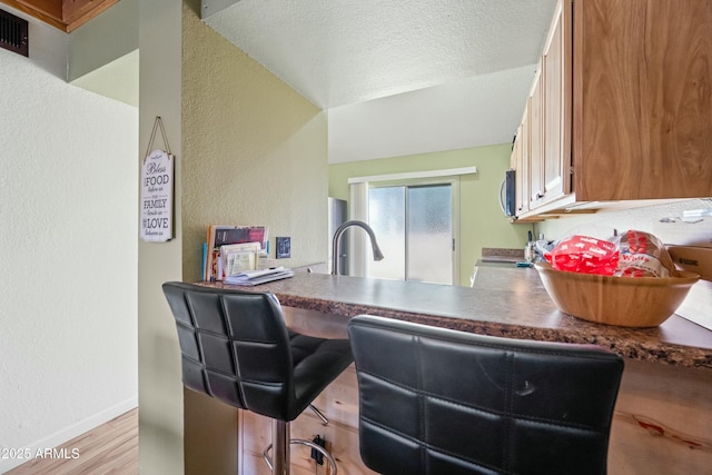 kitchen featuring stainless steel microwave, light wood-style floors, a textured ceiling, range, and baseboards