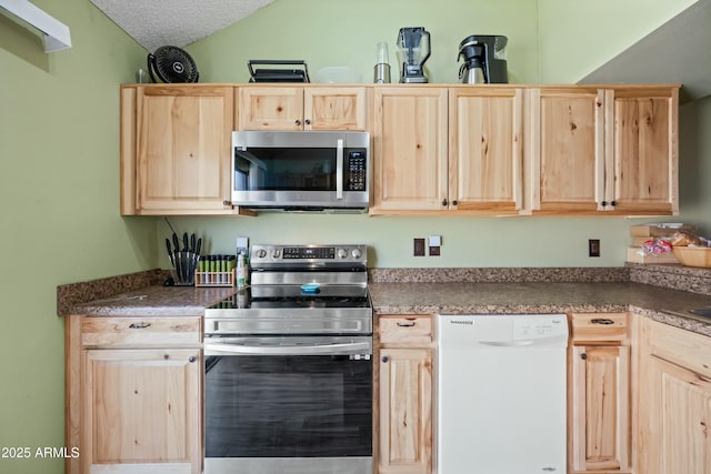 kitchen featuring vaulted ceiling, stainless steel appliances, light brown cabinetry, and a textured ceiling