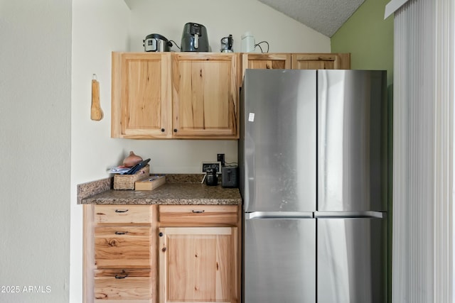 kitchen with dark countertops, light brown cabinetry, freestanding refrigerator, vaulted ceiling, and a textured ceiling