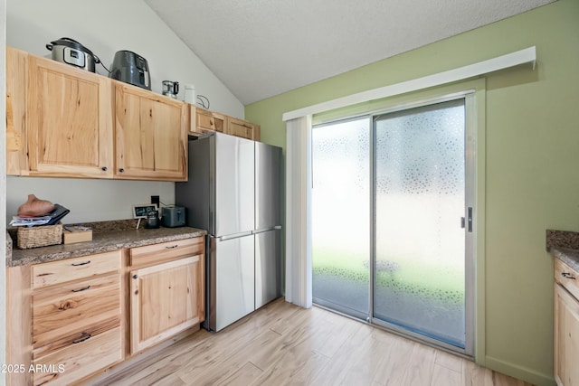 kitchen featuring lofted ceiling, dark countertops, light wood-style flooring, freestanding refrigerator, and light brown cabinetry