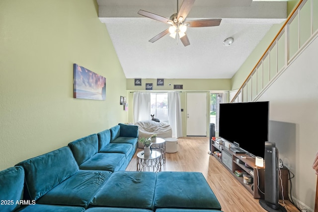 living area featuring vaulted ceiling, a textured ceiling, light wood-style flooring, and a ceiling fan