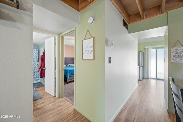 hallway with light wood-type flooring, beam ceiling, visible vents, and baseboards