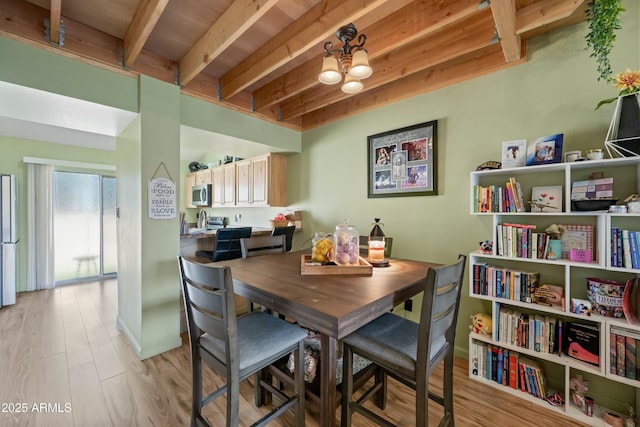 dining area featuring baseboards, beamed ceiling, light wood finished floors, and an inviting chandelier