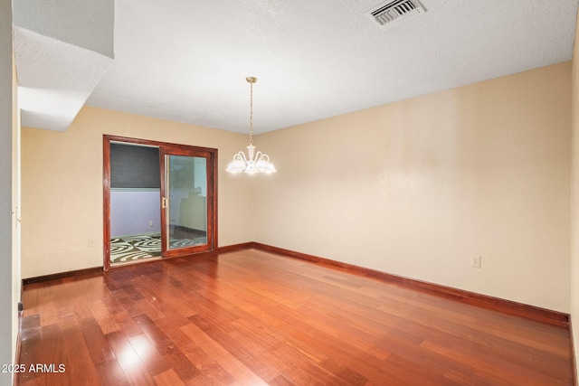 unfurnished room featuring hardwood / wood-style floors, a textured ceiling, and an inviting chandelier