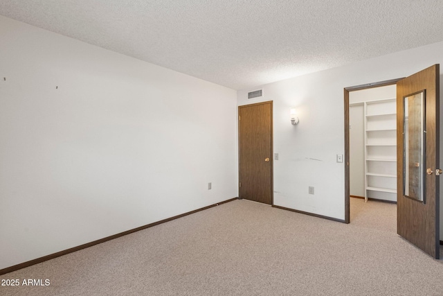 unfurnished bedroom with a spacious closet, light colored carpet, a textured ceiling, and a closet