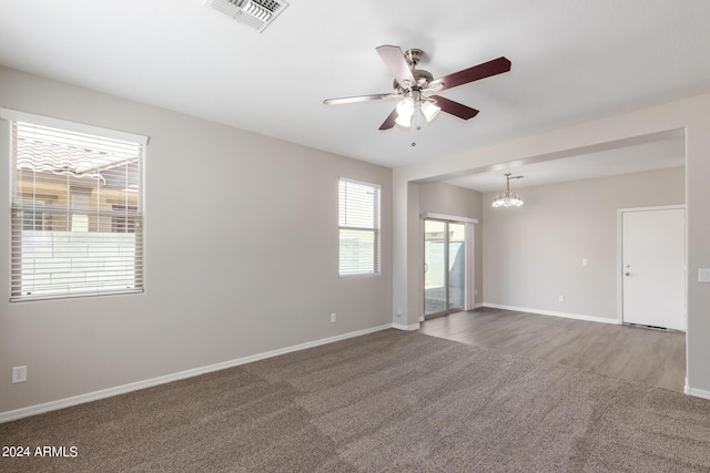carpeted spare room featuring baseboards, visible vents, and ceiling fan with notable chandelier