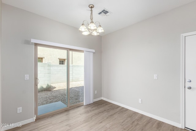 unfurnished room featuring baseboards, visible vents, wood finished floors, and a chandelier