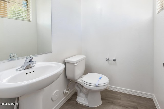 half bath featuring baseboards, toilet, a sink, and wood finished floors