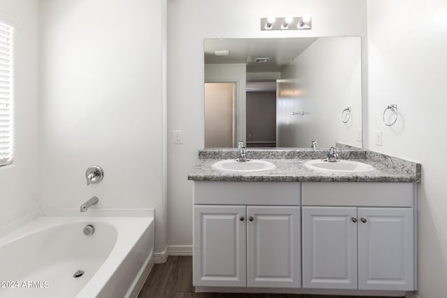 full bath featuring double vanity, a sink, a tub to relax in, and wood finished floors