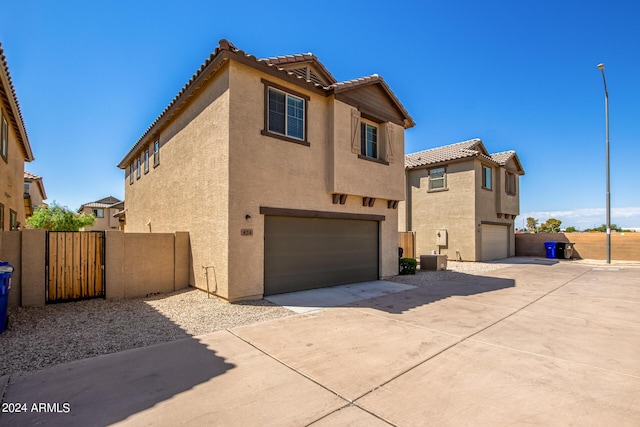 rear view of property featuring stucco siding, a tile roof, a garage, and driveway