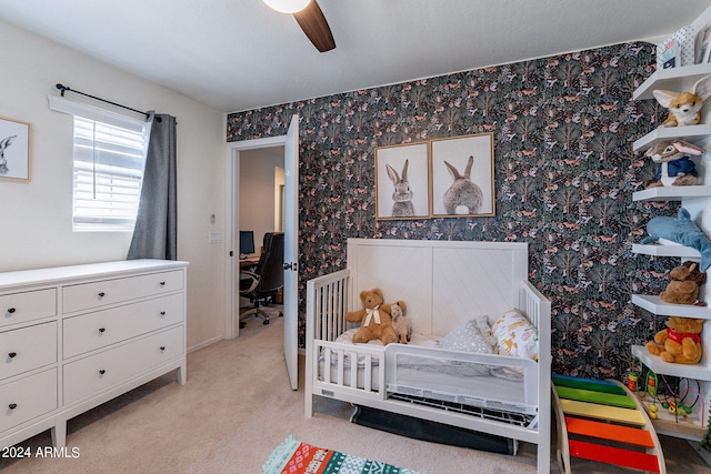 carpeted bedroom with a crib and ceiling fan