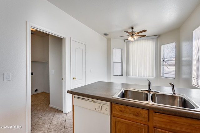 kitchen with light tile patterned floors, dark countertops, brown cabinetry, white dishwasher, and a sink