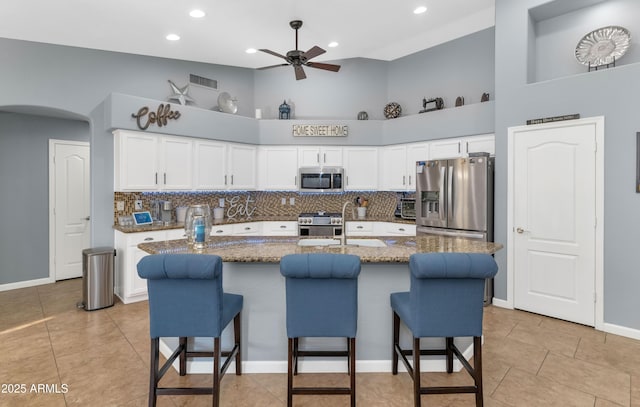 kitchen with sink, appliances with stainless steel finishes, an island with sink, white cabinets, and dark stone counters