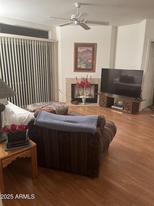 living room with a ceiling fan, wood finished floors, and a tile fireplace