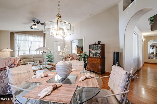 dining area with ceiling fan with notable chandelier, lofted ceiling, and light hardwood / wood-style floors