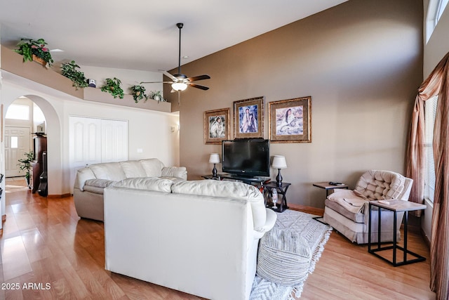 living room featuring light wood-type flooring, ceiling fan, and a towering ceiling