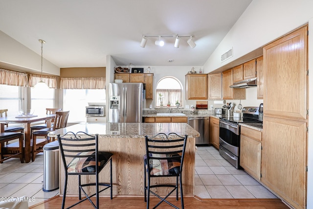 kitchen with lofted ceiling, light tile patterned floors, appliances with stainless steel finishes, and a center island