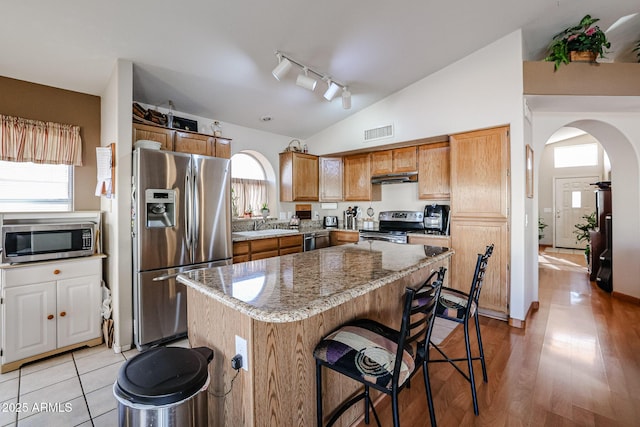 kitchen with a center island, stainless steel appliances, stone countertops, vaulted ceiling, and a breakfast bar