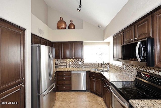 kitchen featuring lofted ceiling, backsplash, sink, light stone countertops, and appliances with stainless steel finishes