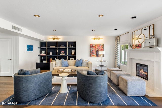 living area featuring a glass covered fireplace, recessed lighting, wood finished floors, and visible vents