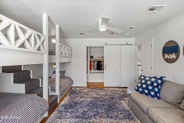 bedroom with a barn door, wood finished floors, visible vents, and a textured ceiling