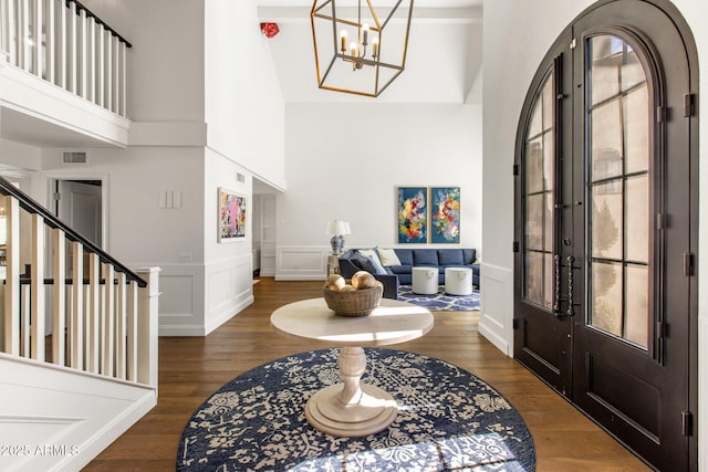 entryway featuring wood finished floors, a wainscoted wall, a towering ceiling, a decorative wall, and a notable chandelier