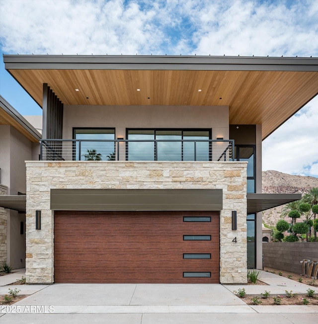 contemporary house featuring a balcony, stone siding, driveway, and a garage