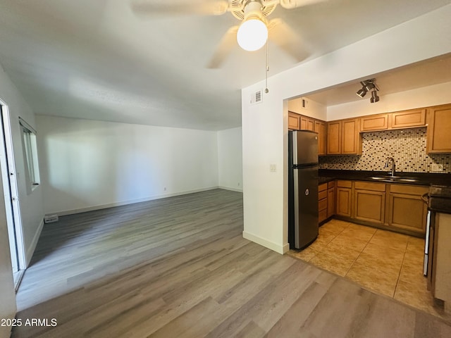 1702 W Tuckey Ln Unit 116, Phoenix, AZ 85015 - kitchen with freestanding refrigerator, dark countertops, light wood-style floors, ceiling fan, and brown cabinetry