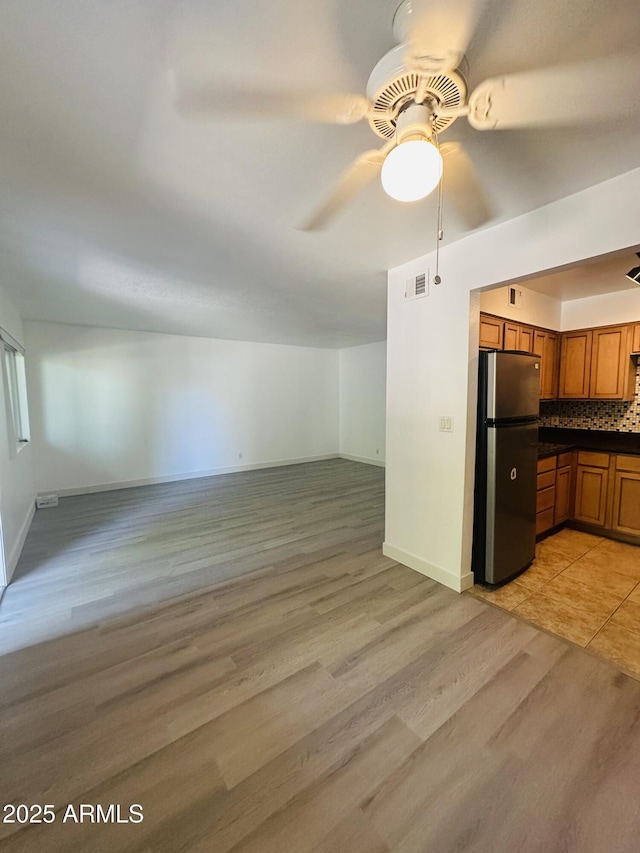 1702 W Tuckey Ln Unit 116, Phoenix, AZ 85015 - kitchen with freestanding refrigerator, brown cabinetry, ceiling fan, light wood-style flooring, and dark countertops