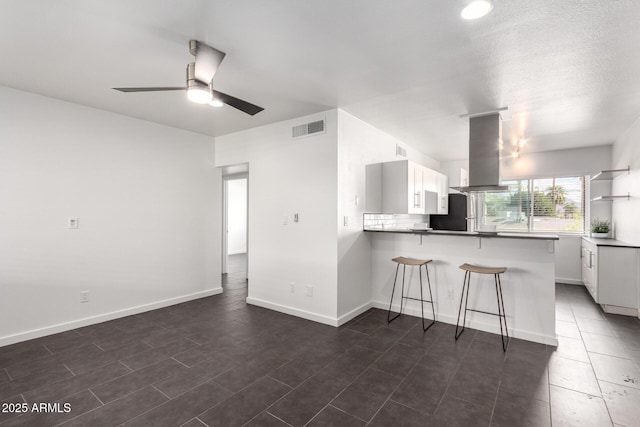 kitchen featuring island exhaust hood, visible vents, a peninsula, and white cabinetry