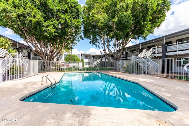 community pool with a patio area, stairs, and fence