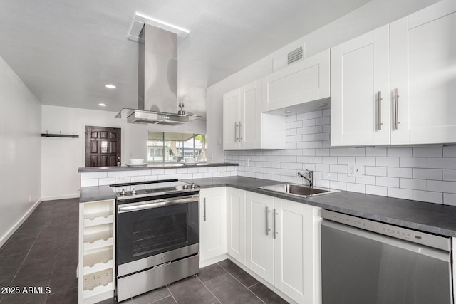 kitchen with dark countertops, a sink, wall chimney range hood, appliances with stainless steel finishes, and dark tile patterned flooring