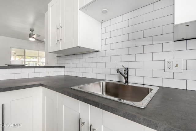 kitchen with dark countertops, white cabinets, backsplash, and a sink