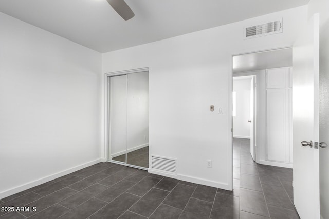 unfurnished bedroom featuring visible vents, baseboards, dark tile patterned flooring, and a closet