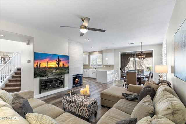 living area with stairway, visible vents, a fireplace, ceiling fan with notable chandelier, and light wood-type flooring