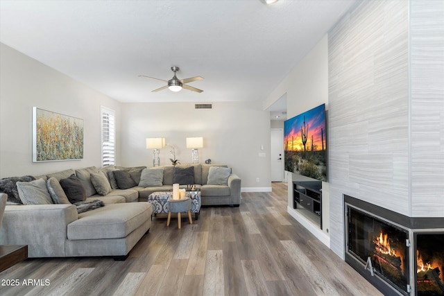 living room featuring visible vents, baseboards, a fireplace, wood finished floors, and a ceiling fan