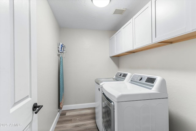 washroom featuring visible vents, baseboards, washing machine and dryer, wood finished floors, and cabinet space