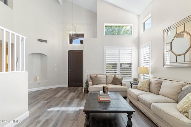 living area with wood finished floors, visible vents, baseboards, high vaulted ceiling, and a notable chandelier