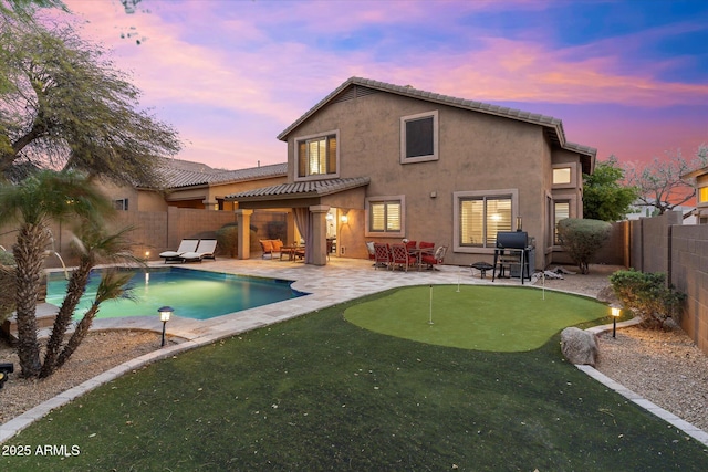 back of property at dusk featuring a patio, a fenced in pool, a fenced backyard, stucco siding, and a tile roof