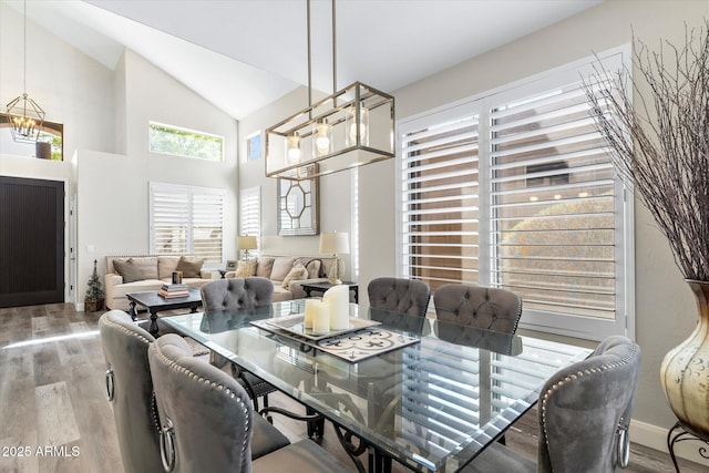 dining area with high vaulted ceiling, an inviting chandelier, and wood finished floors