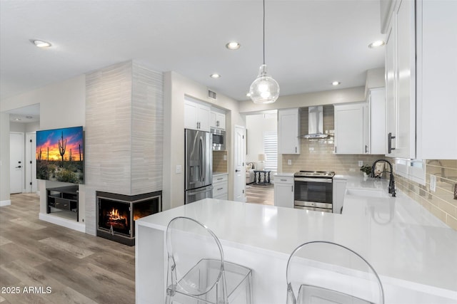 kitchen with a sink, appliances with stainless steel finishes, a fireplace, wall chimney range hood, and decorative backsplash