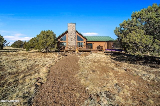 back of house with a trampoline, a wooden deck, metal roof, and a chimney