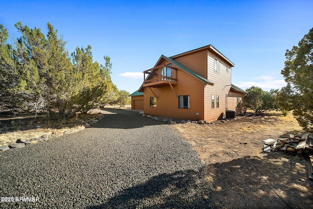 view of side of property with central AC unit, a garage, driveway, and a balcony