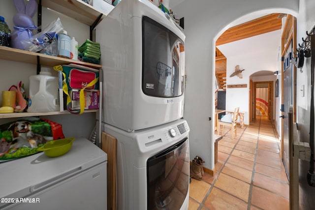laundry area with stacked washer and dryer, arched walkways, light tile patterned flooring, and laundry area