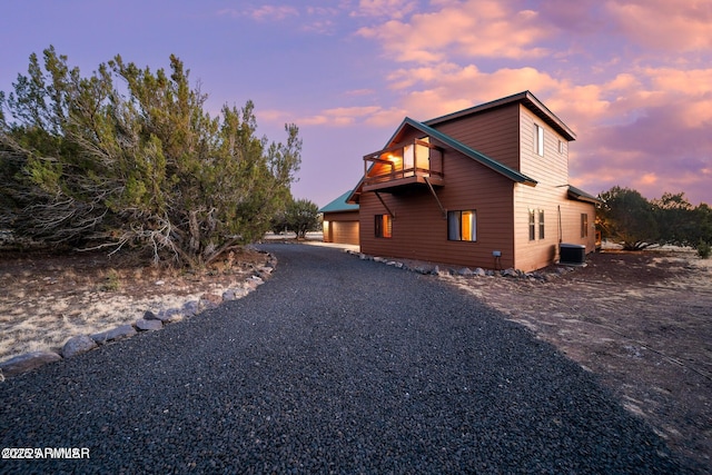 view of property exterior featuring gravel driveway, central AC unit, and a balcony