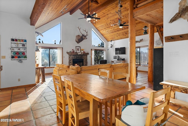 dining area with a wealth of natural light, a stone fireplace, beamed ceiling, and a ceiling fan