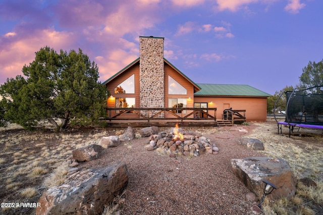 back of property featuring an outdoor fire pit, a trampoline, a wooden deck, and a chimney