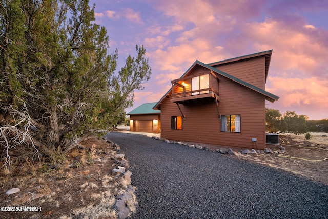 view of front of house with a garage, gravel driveway, and a balcony