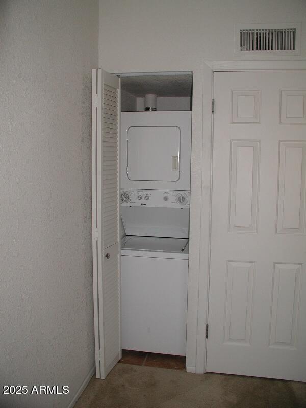 clothes washing area featuring stacked washer / drying machine, laundry area, and visible vents